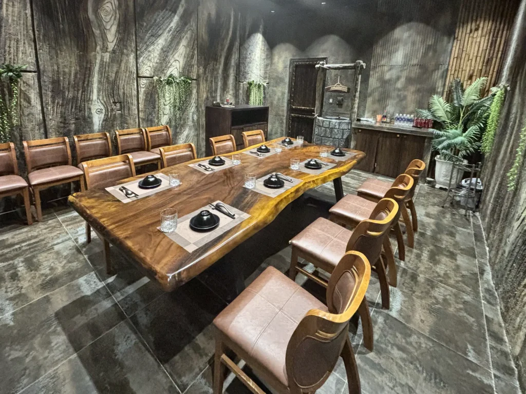 Phòng VIP 01 (Hồng Châu) tại Gánh Ngon: bàn gỗ dài, ghế bọc nệm nâu, tường giả vân gỗ xám và cây xanh