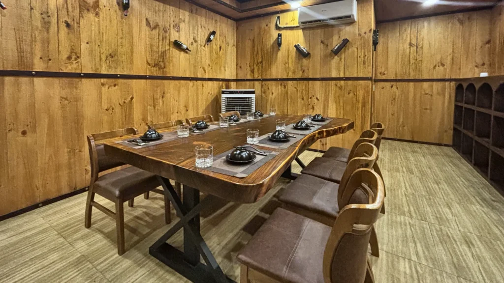 Phòng VIP 08 (Đảo Ngọc) tại Gánh Ngon: tường ốp gỗ, sàn gỗ sáng màu, bàn gỗ dài và ghế bọc nệm nâu