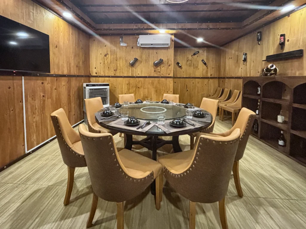 Phòng VIP 09 (Kim Châu) tại Gánh Ngon: bàn tròn có mâm xoay kính, ghế bọc nệm màu bò, tường ốp gỗ và kệ gỗ