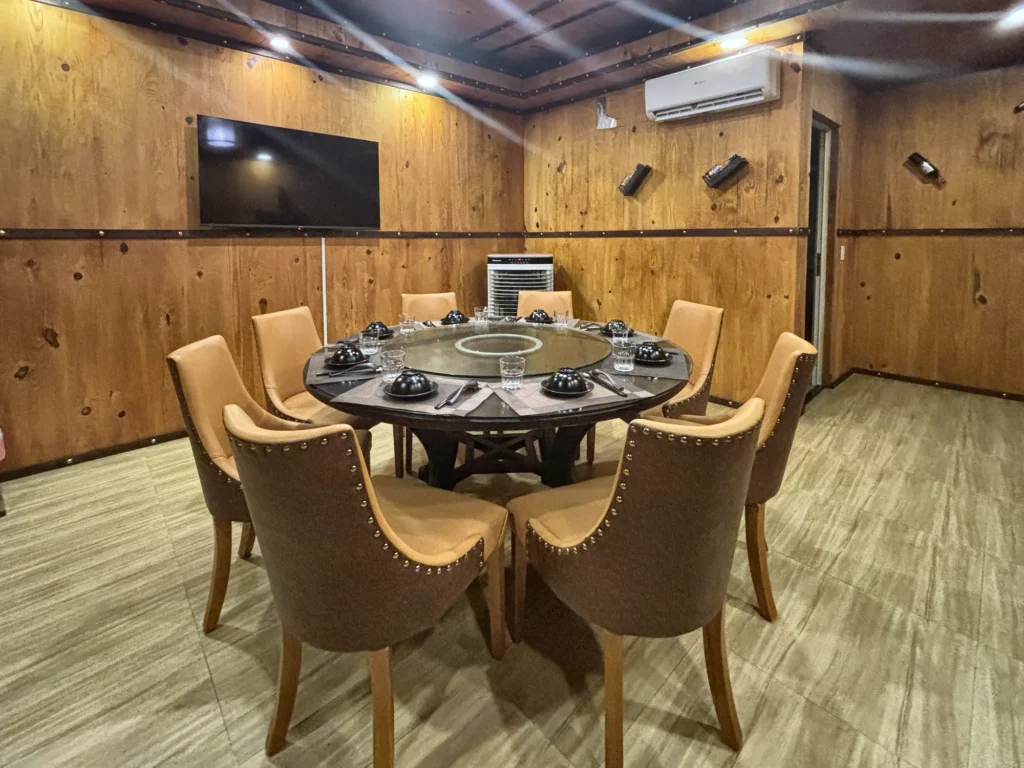 Phòng VIP 09 (Kim Châu) tại Gánh Ngon: bàn tròn có mâm xoay kính, ghế bọc nệm màu bò, tường ốp gỗ và kệ gỗ
